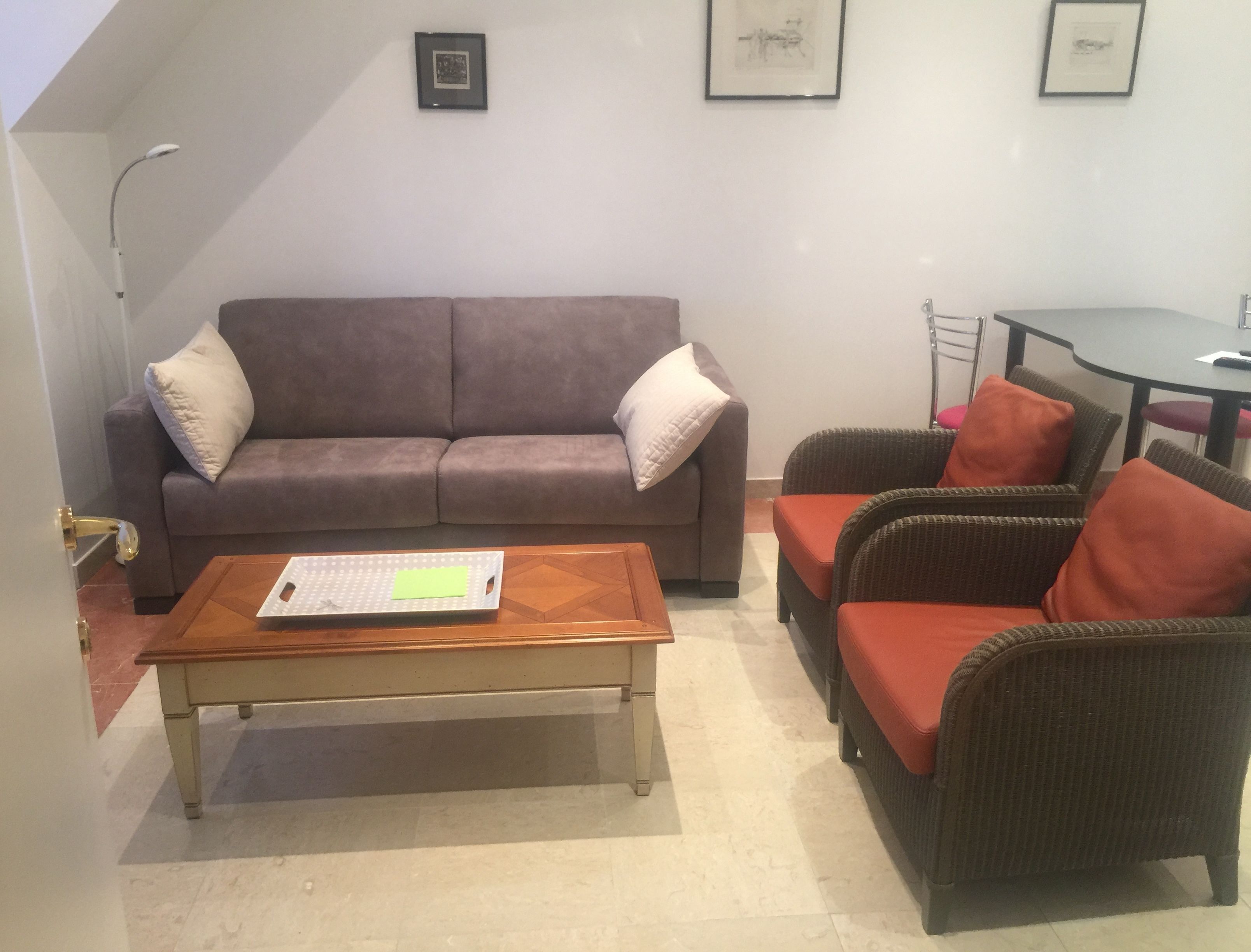 Un salon avec un canapé marron, deux fauteuils, une table basse en bois et une petite table accompagnée d’une chaise.