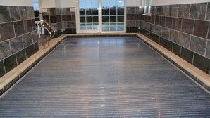 A large indoor swimming pool with a tiled floor and walls, a metal handrail, and a door leading outside. - PS Orion (De Haan)