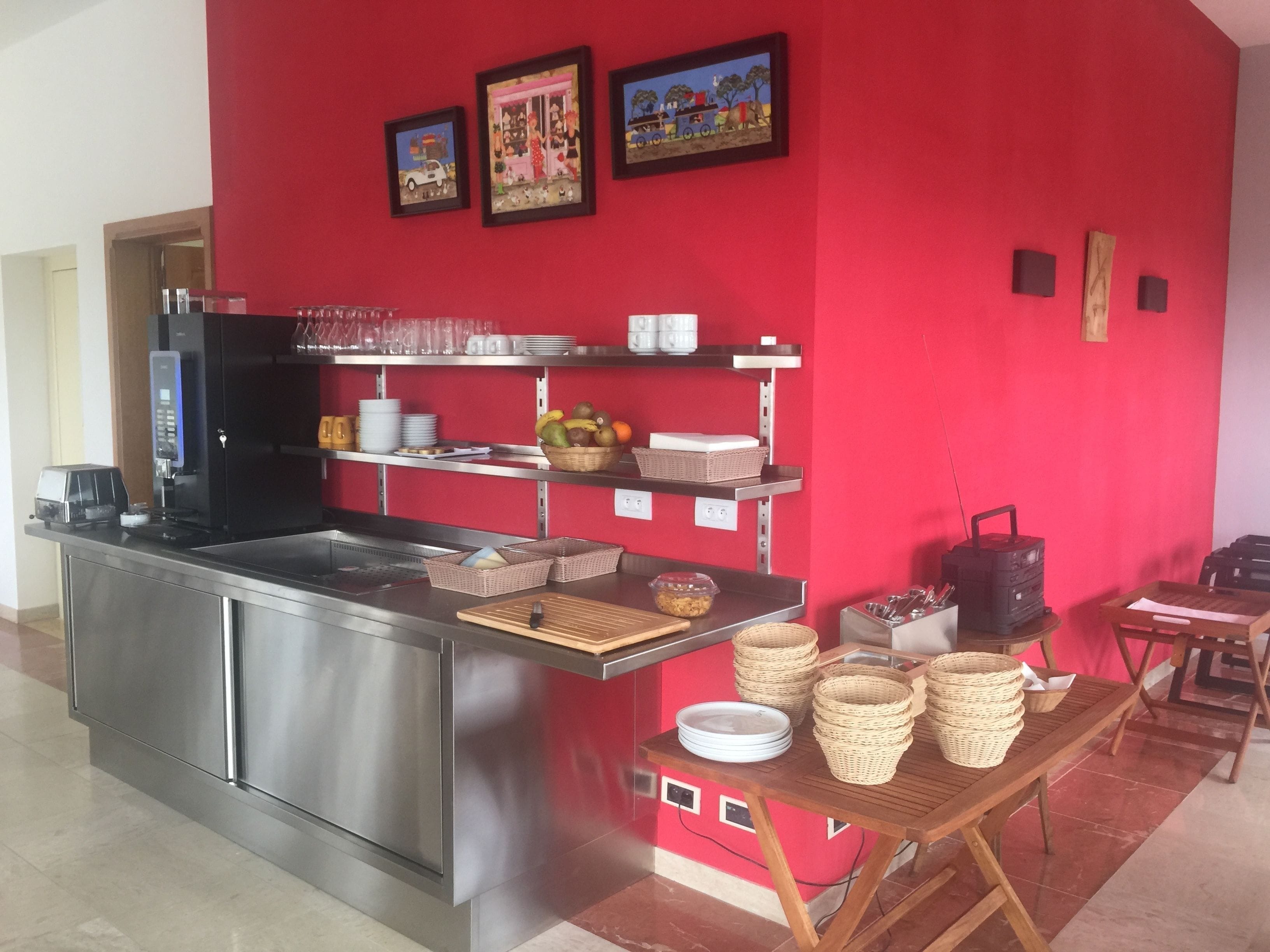 A kitchen area with stainless steel appliances, a red wall with framed artwork, and a buffet setup with baskets and plates.