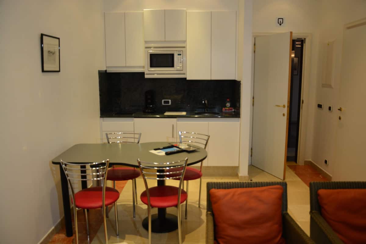 Een kleine keuken met een magnetron, koffiezetapparaat en een eettafel met stoelen.