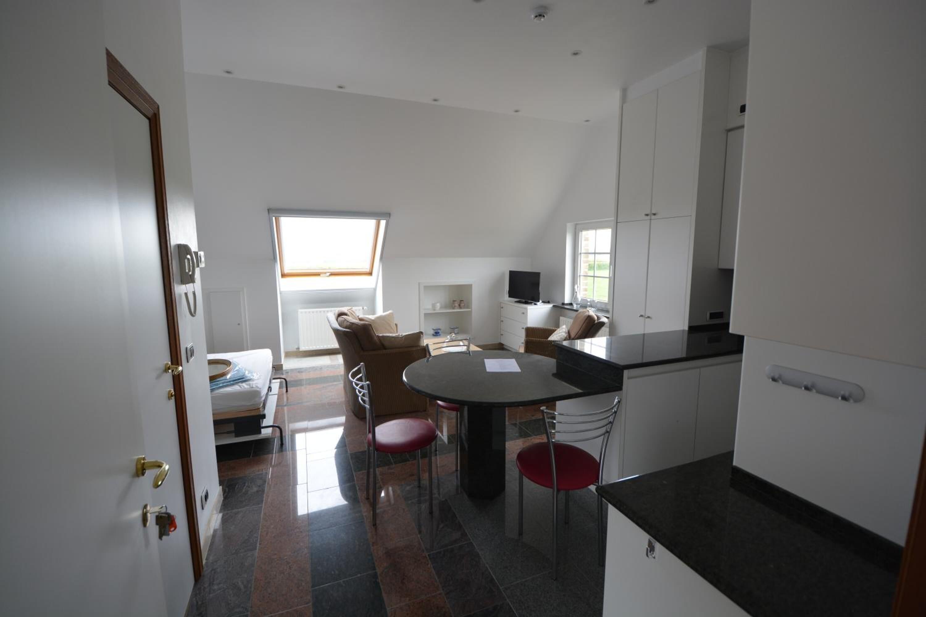 A modern kitchen with a dining area, white cabinets, a black countertop, and a window providing natural light.