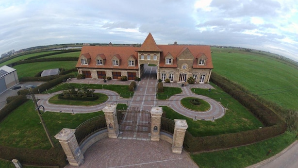 A large, historic building with a central entrance, surrounded by well-maintained lawns and a paved driveway. - PS Orion (De Haan)