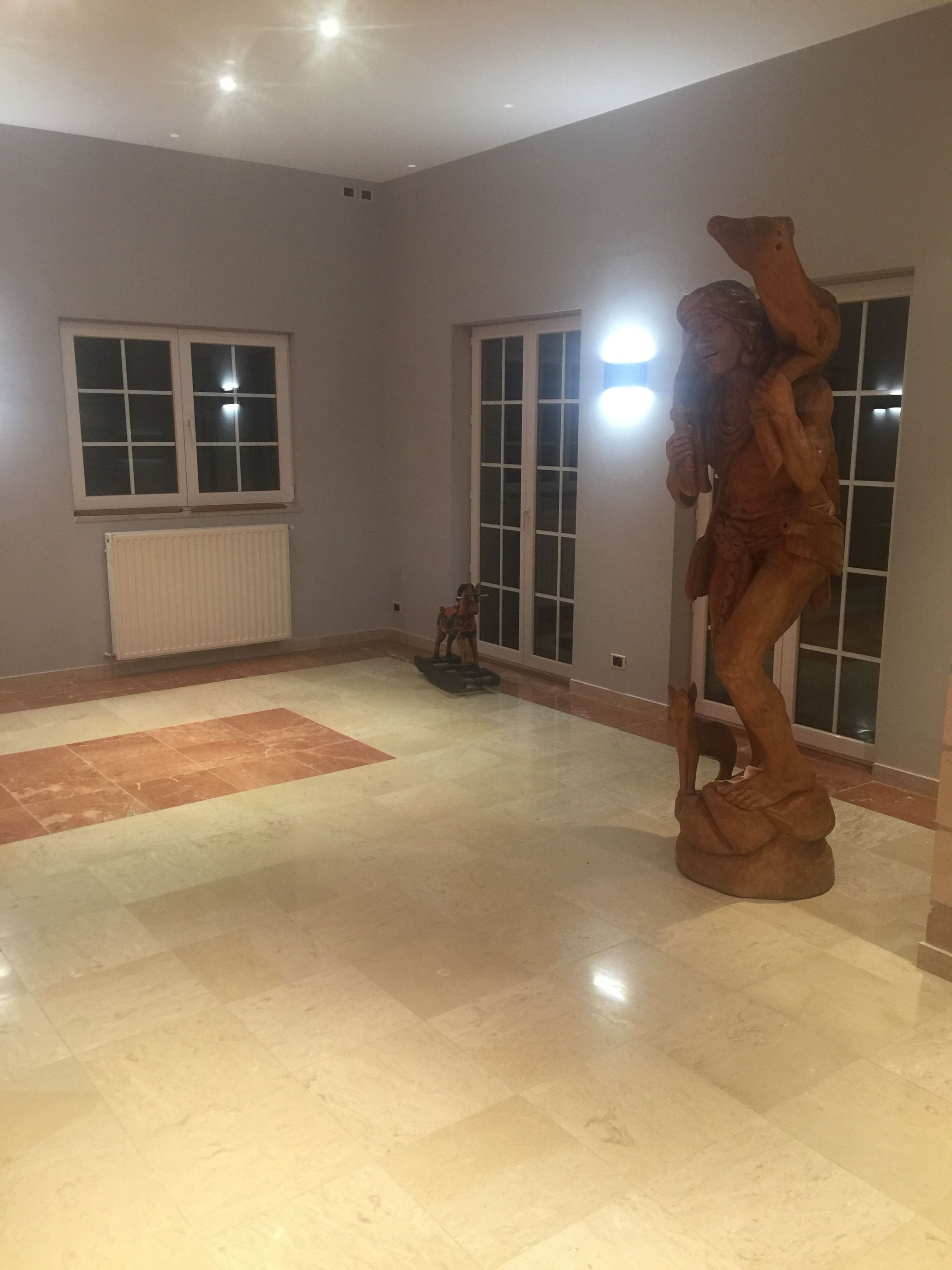 A spacious room with a large wooden sculpture, a radiator, and a window with blinds.