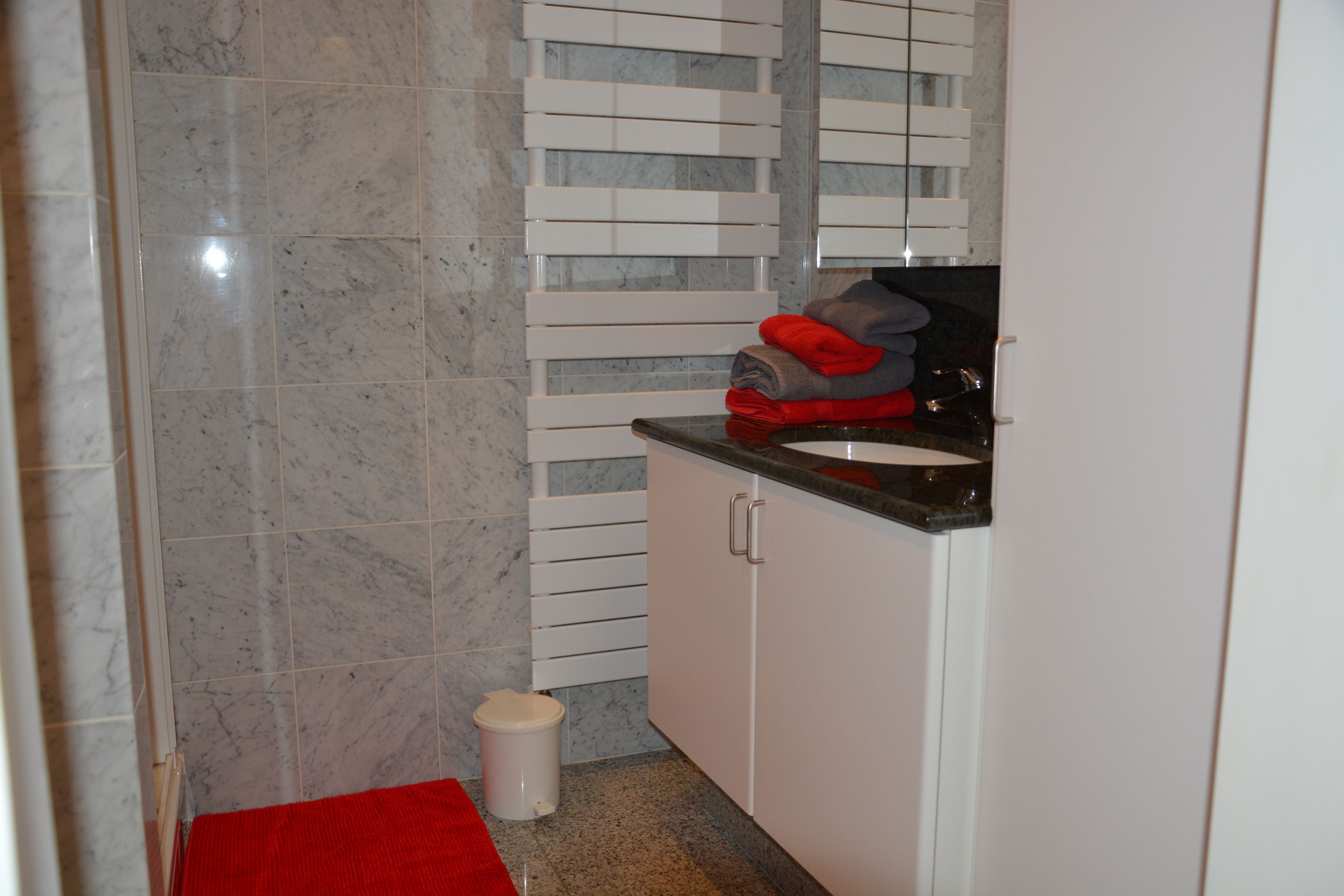 A bathroom with a marble floor, white cabinets, a sink, and a red towel on the counter.