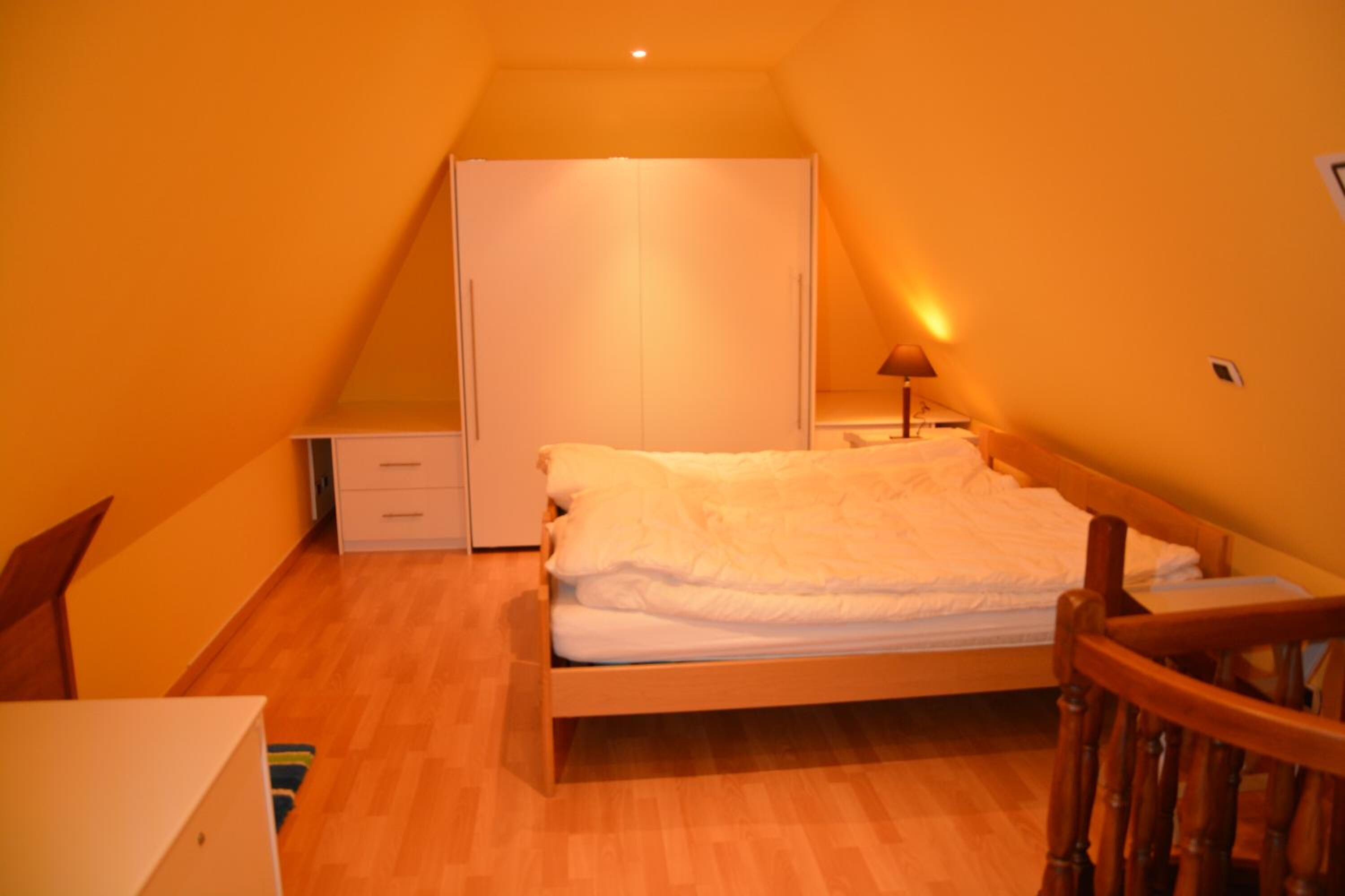 Une petite chambre confortable, avec un lit simple, une chaise en bois, un bureau et une armoire.