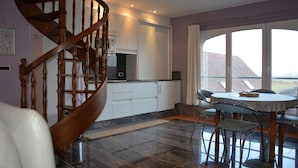 A modern kitchen with a wooden staircase, a dining area with a table and chairs, and a large window offering a view of the outside. - PS Orion (De Haan)