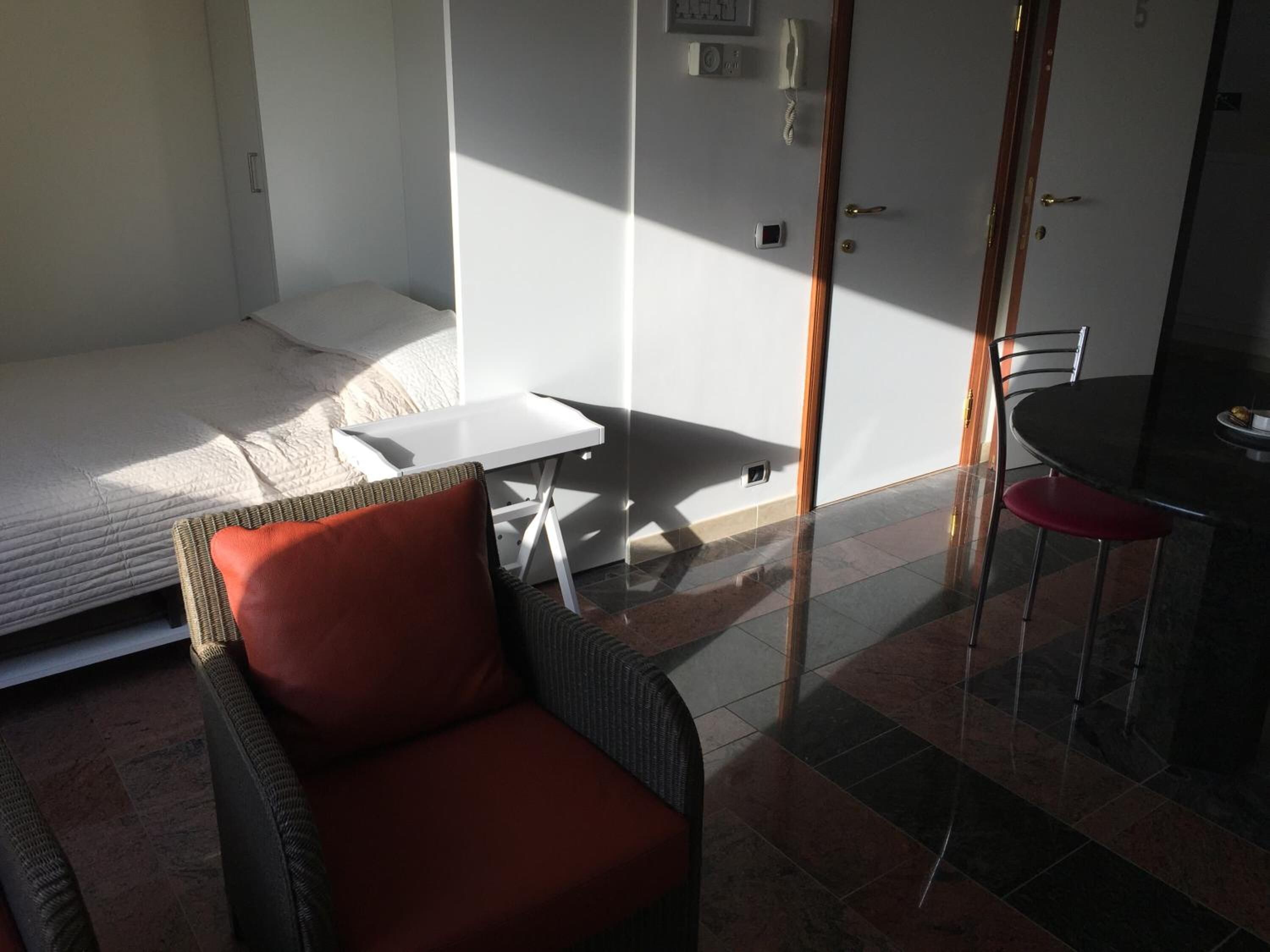 Ein gemütlicher Raum mit Bett, kleinem Tisch, Korbsessel und Esstisch mit Stühlen.