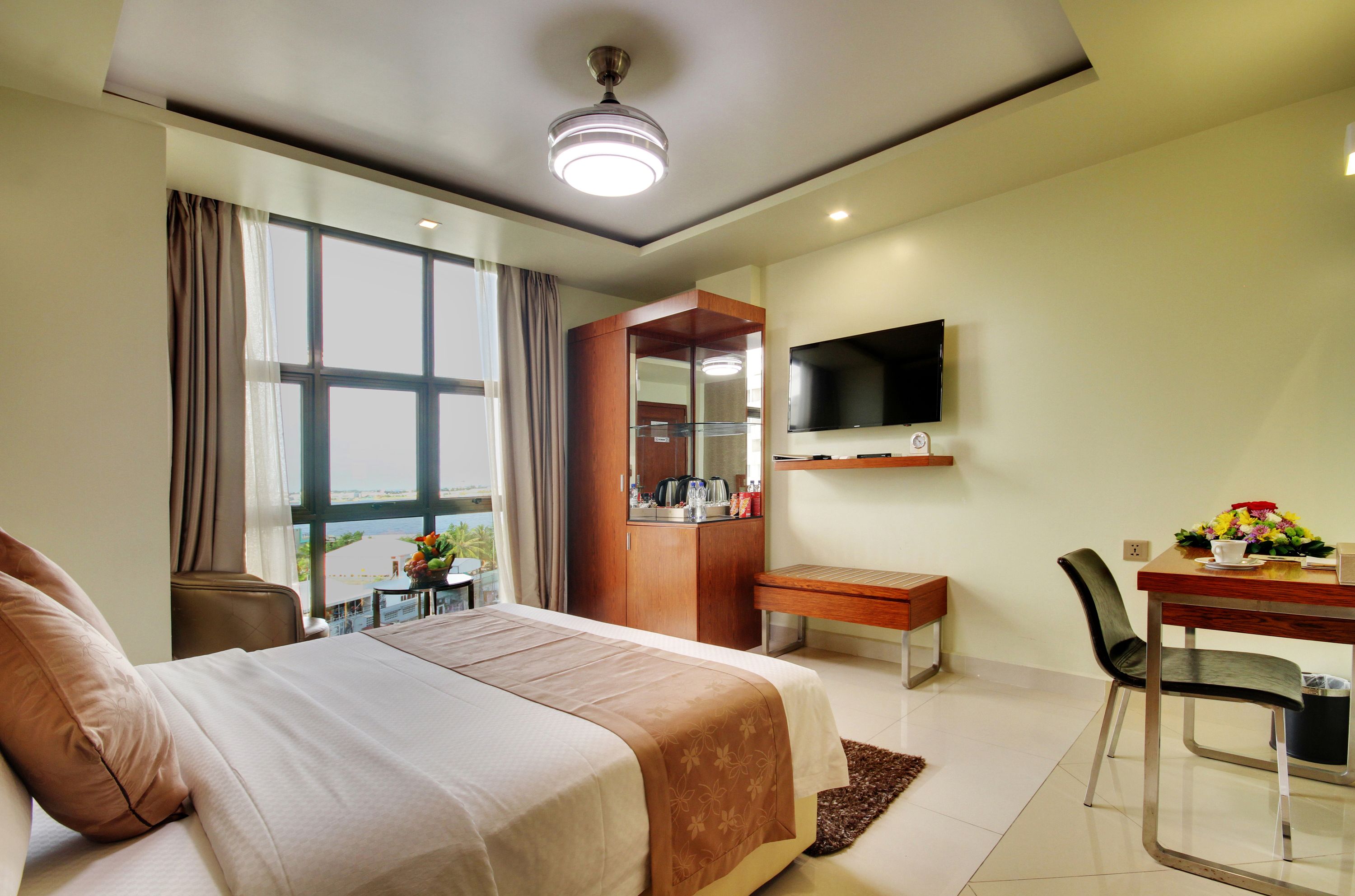 Ein Hotelzimmer mit einem großen Bett, einem Schreibtisch mit Stuhl, einem an der Wand befestigten Fernseher und einem Fenster mit Vorhängen.