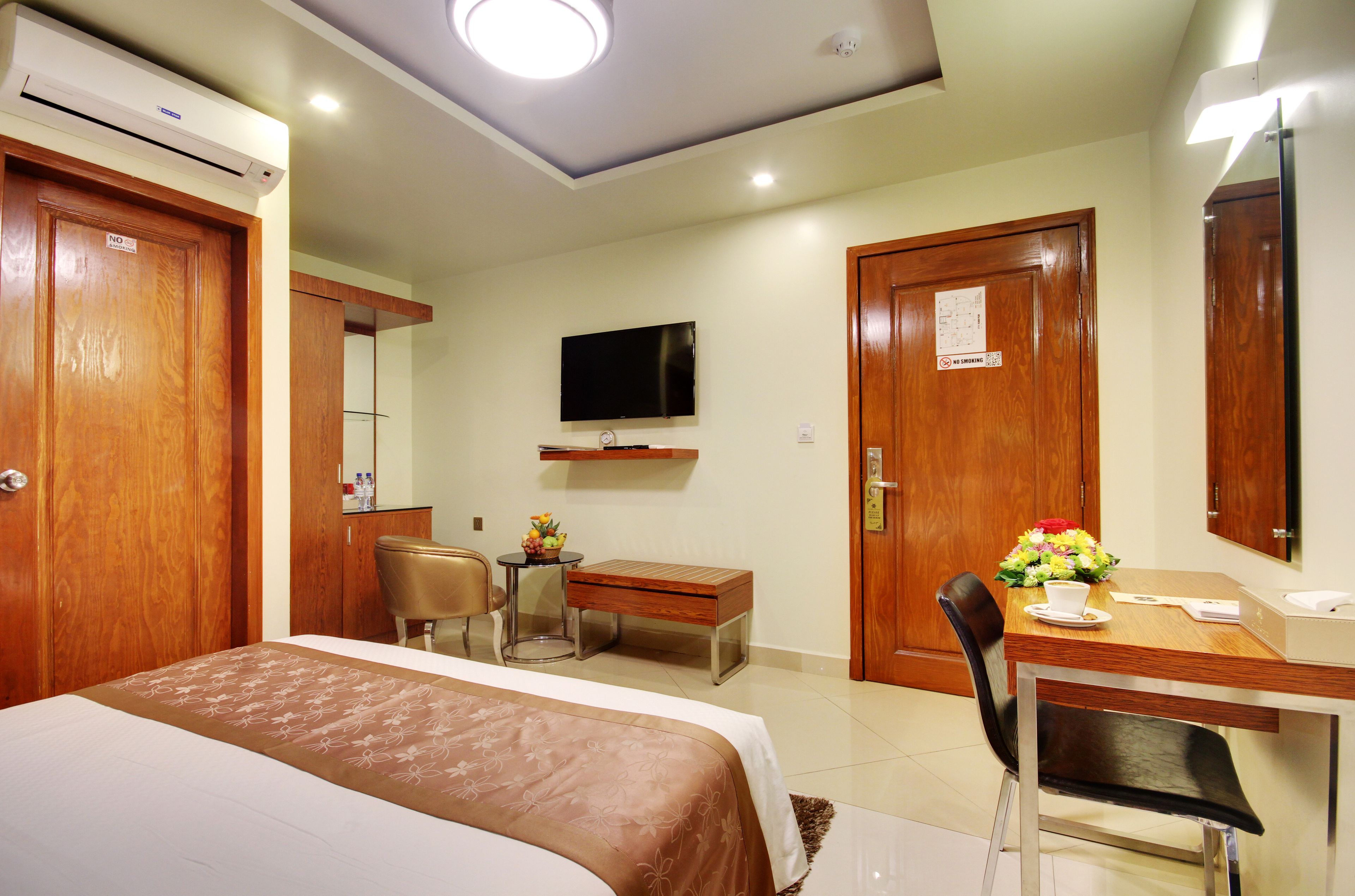 A hotel room with a bed, a desk, a chair, a television, and a mirror.