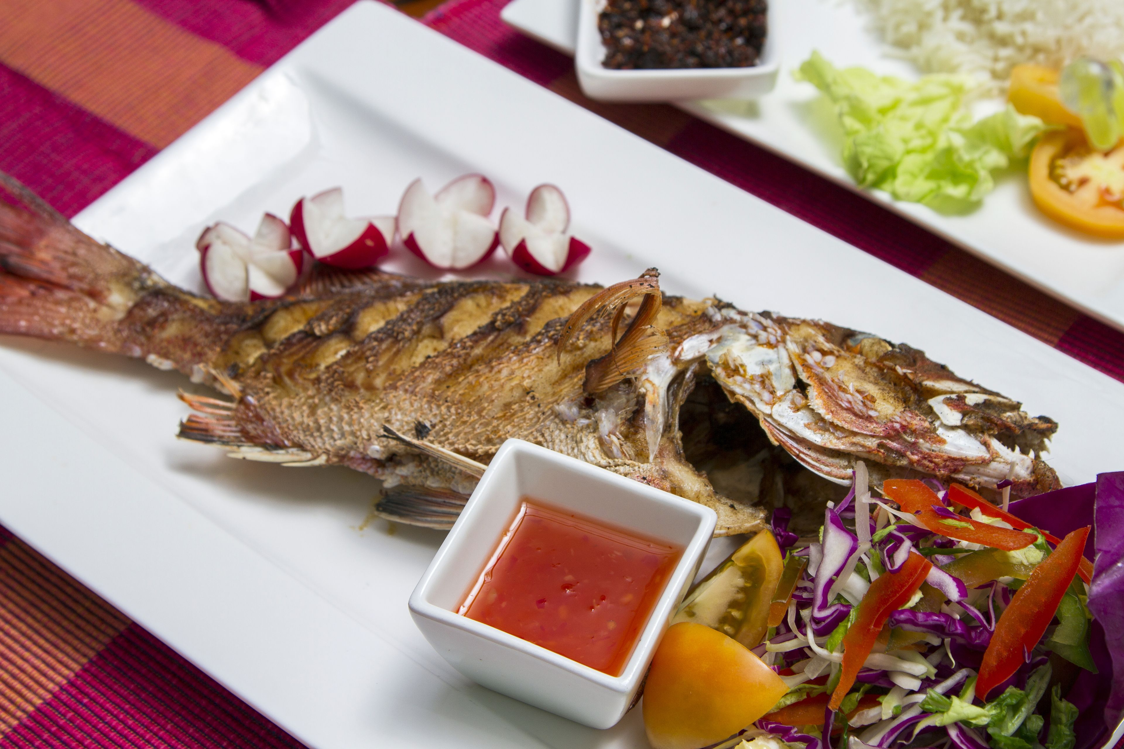 Pesce alla griglia su un piatto bianco, accompagnato da un'insalata e da ravanelli a fettine.
