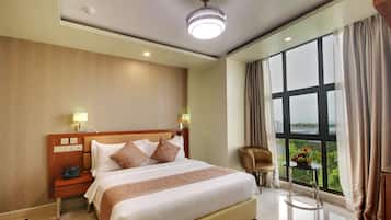 Habitación de hotel con una cama grande, lámparas de noche, una mesita con frutero, una silla y vista a zonas verdes por la ventana.