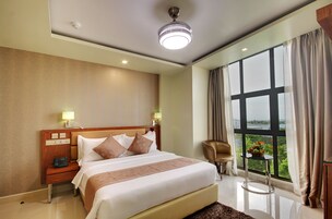 Habitación de hotel con una cama grande, lámparas de noche, una mesita con frutero, una silla y vista a zonas verdes por la ventana.