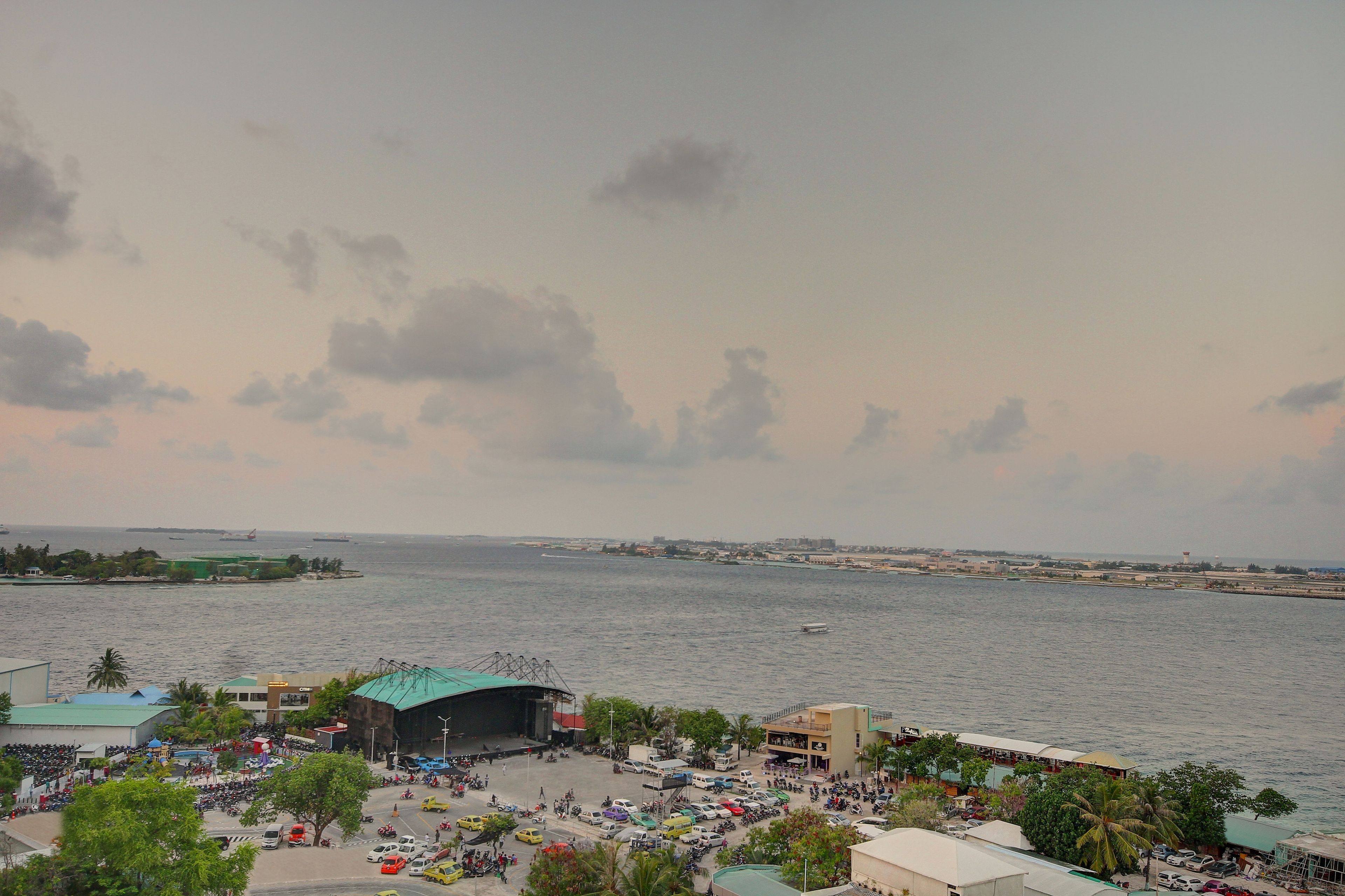 A waterfront area with a stage and seating for events, a parking lot, and a view of the sea.