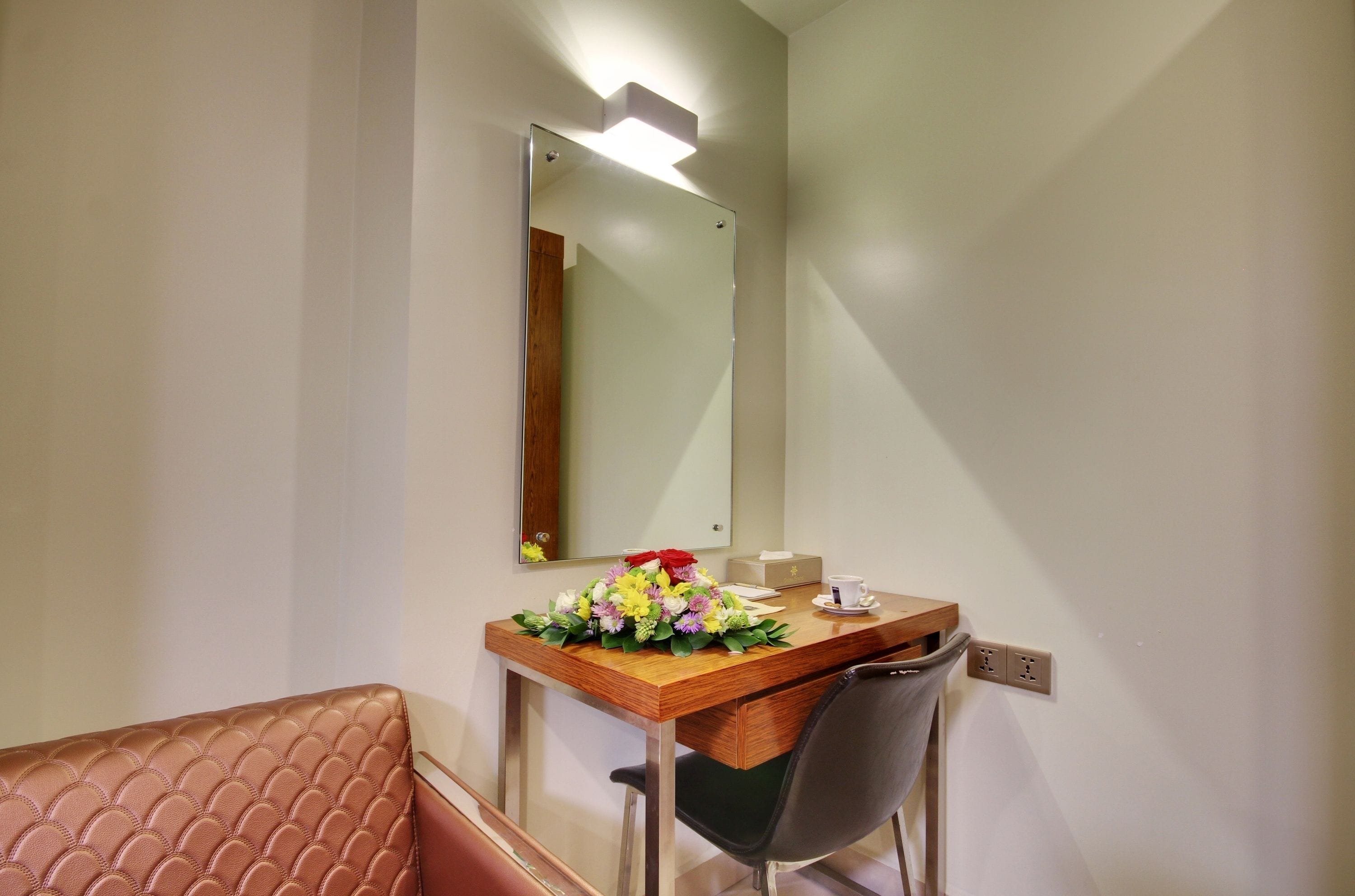 Una habitación de hotel con un escritorio de madera, una silla, un espejo y un arreglo floral.