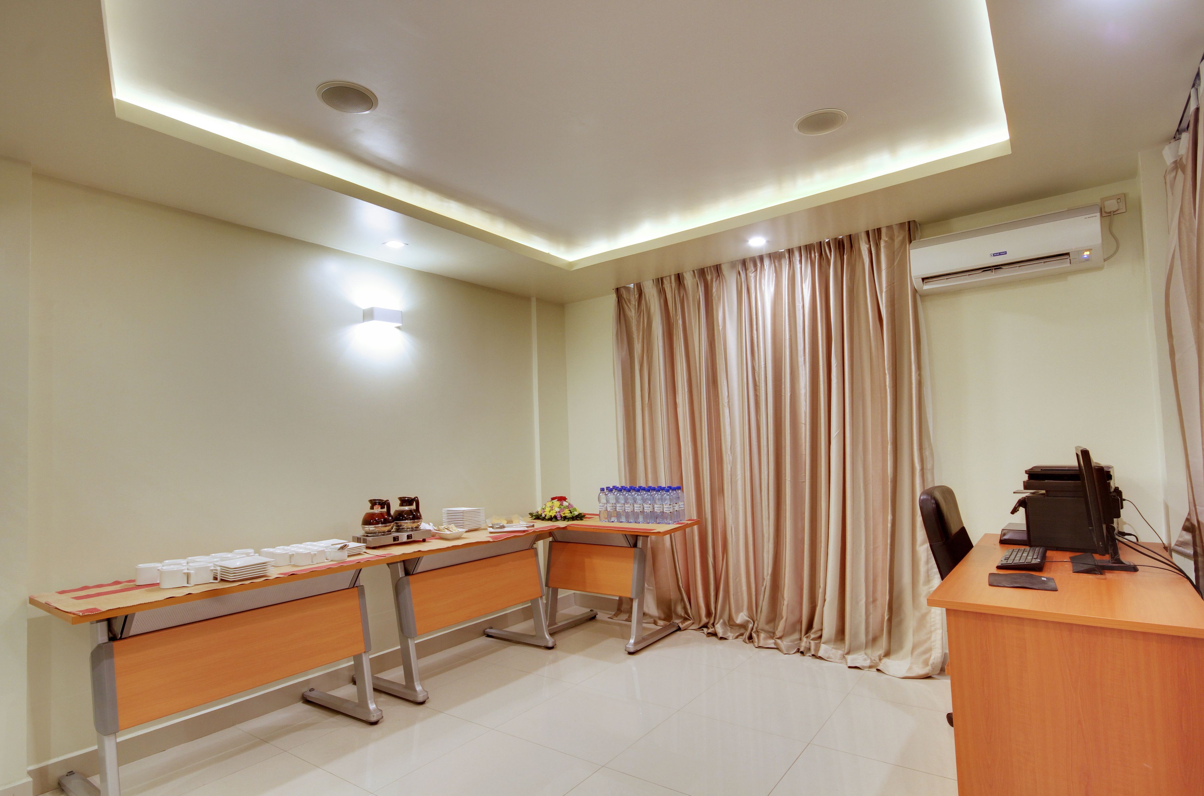 A conference room with a long table, chairs, a desk with a computer, and an air conditioning unit.