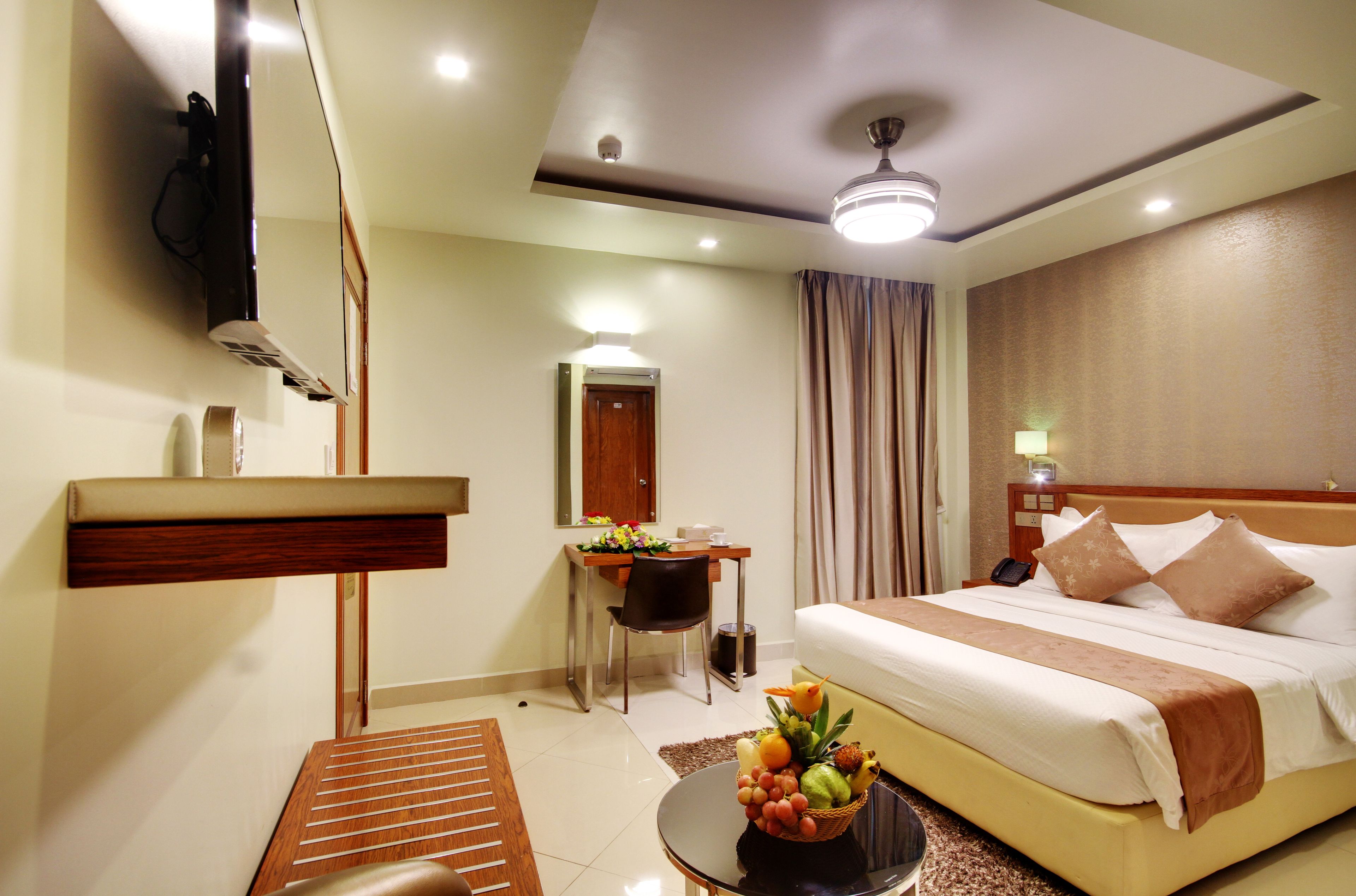A hotel room with a bed, bedside table, desk, chair, and a small table with fruit.
