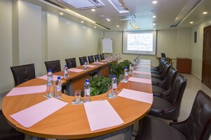 Un salón de conferencias con una larga mesa, sillas, botellas de agua y una pantalla para presentaciones.