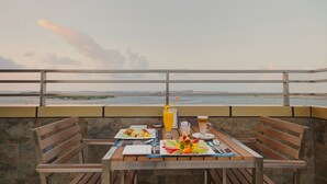 Una mesa con platos de comida, un vaso de jugo de naranja y una jarra de cerveza, frente a una vista panorámica del mar.