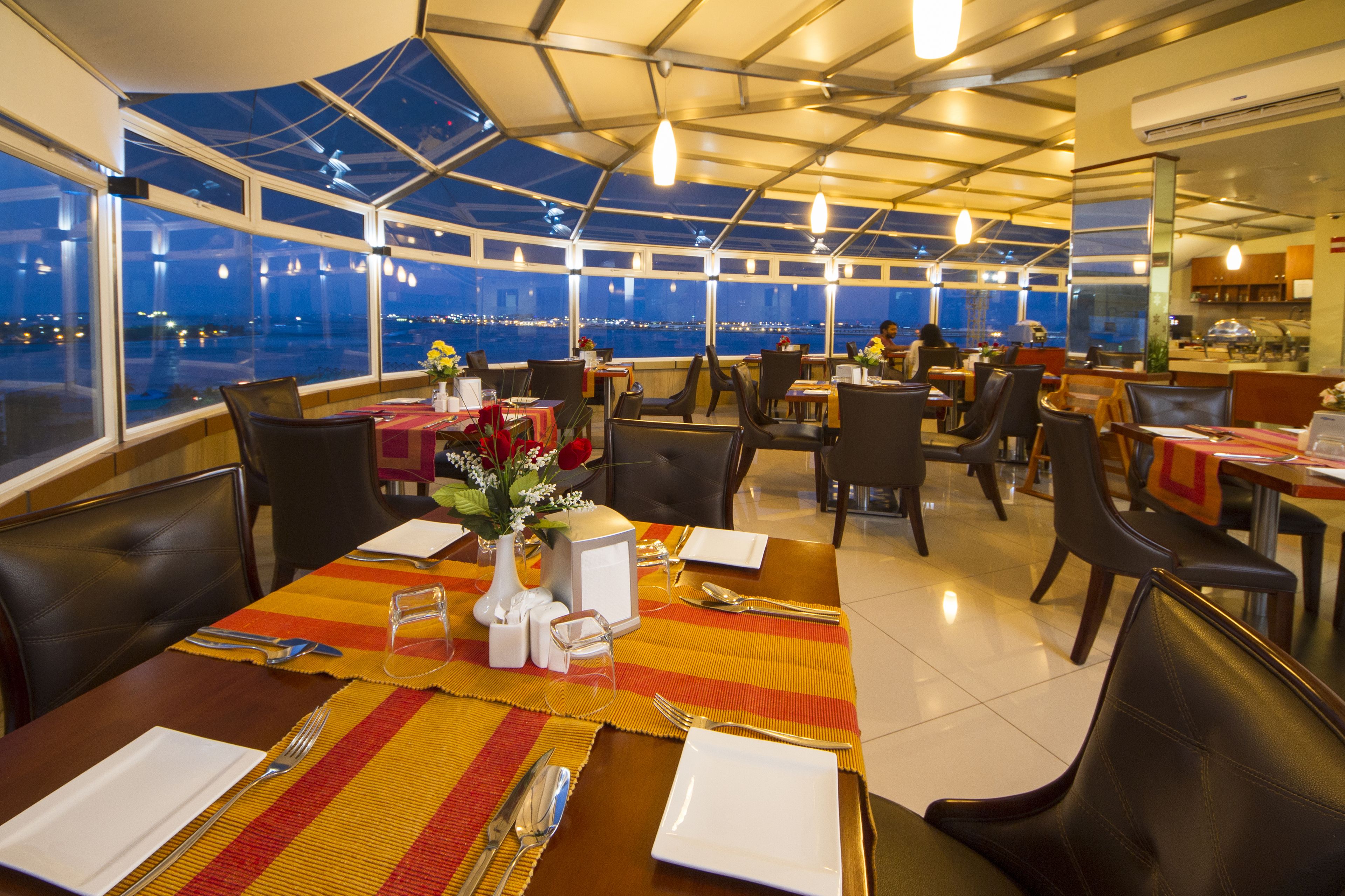 A restaurant with tables set for dining, large windows offering a view of the city at night, and a modern interior design.