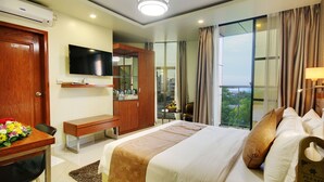 Una habitación de hotel con una cama, un escritorio con una silla, un televisor montado en la pared, un armario y una ventana con cortinas.