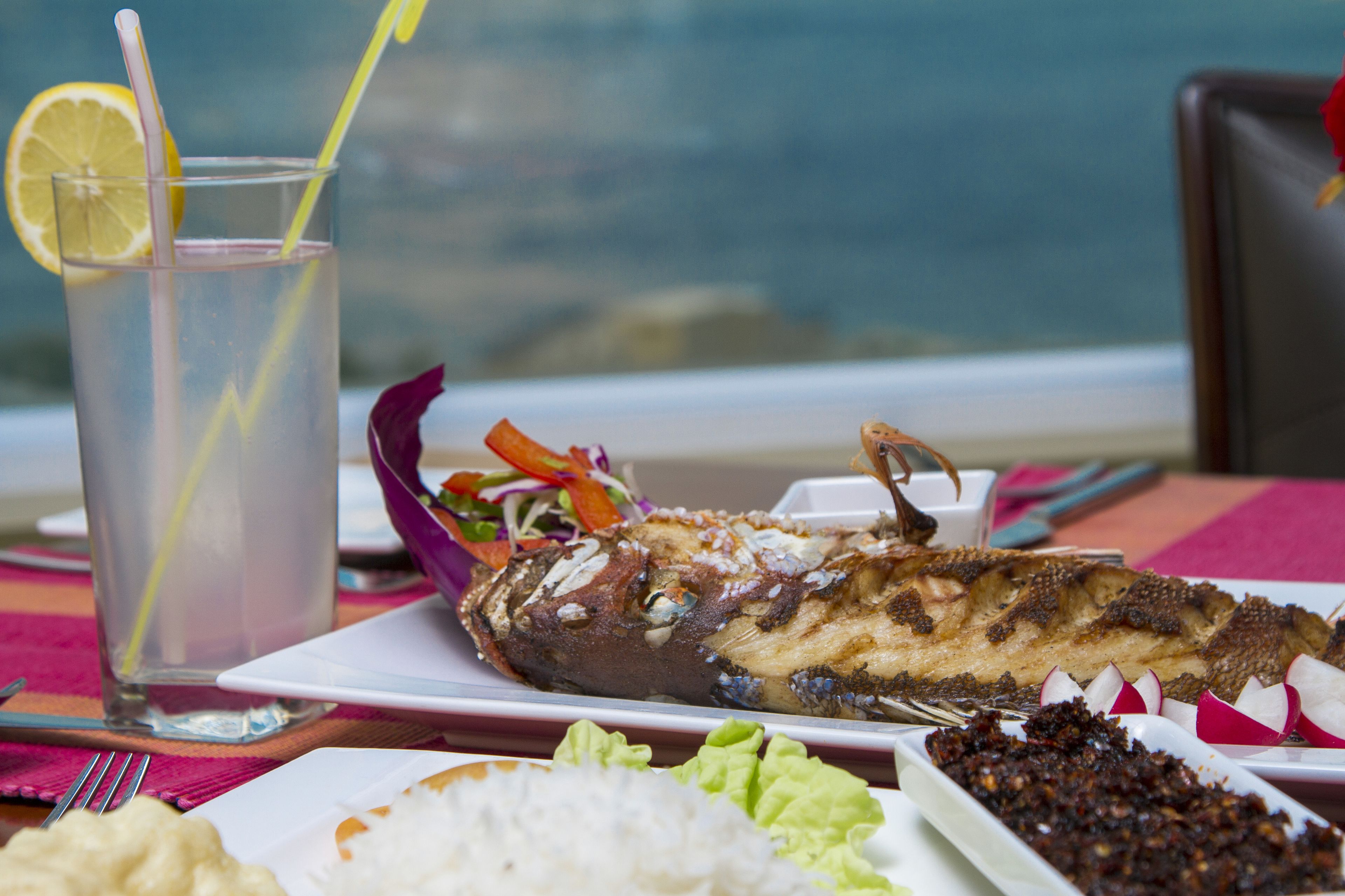 A table with a fish dish, a glass of water, and various side dishes.