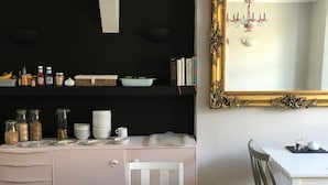 A dining area with a white table and chairs, a black wall with a gold-framed mirror, and a shelf with kitchen items.