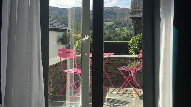 A room with a sliding glass door leading to an outdoor patio with pink chairs and a table.