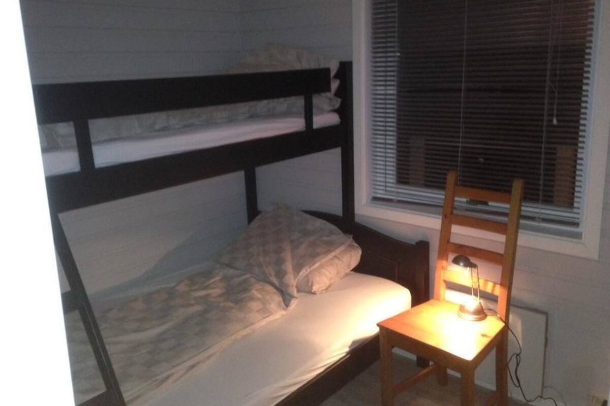 Una cama individual con cabecera de madera, una mesita de noche con lámpara y una ventana con persianas.
