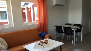 A compact living space with a sofa, a small table with a glass, and a dining area with chairs and a table.
