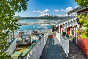 A waterfront property with a deck, outdoor seating, and a view of a lake and mountains. - Garsnes Brygge (Salangen)