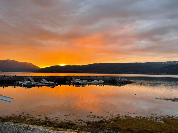 A marina with boats docked, calm water, and a sunset over mountains. - Garsnes Brygge (Salangen)