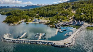 Vue aérienne d’une propriété au bord du lac, avec un quai, des bateaux et des maisons, le tout entouré de collines boisées.