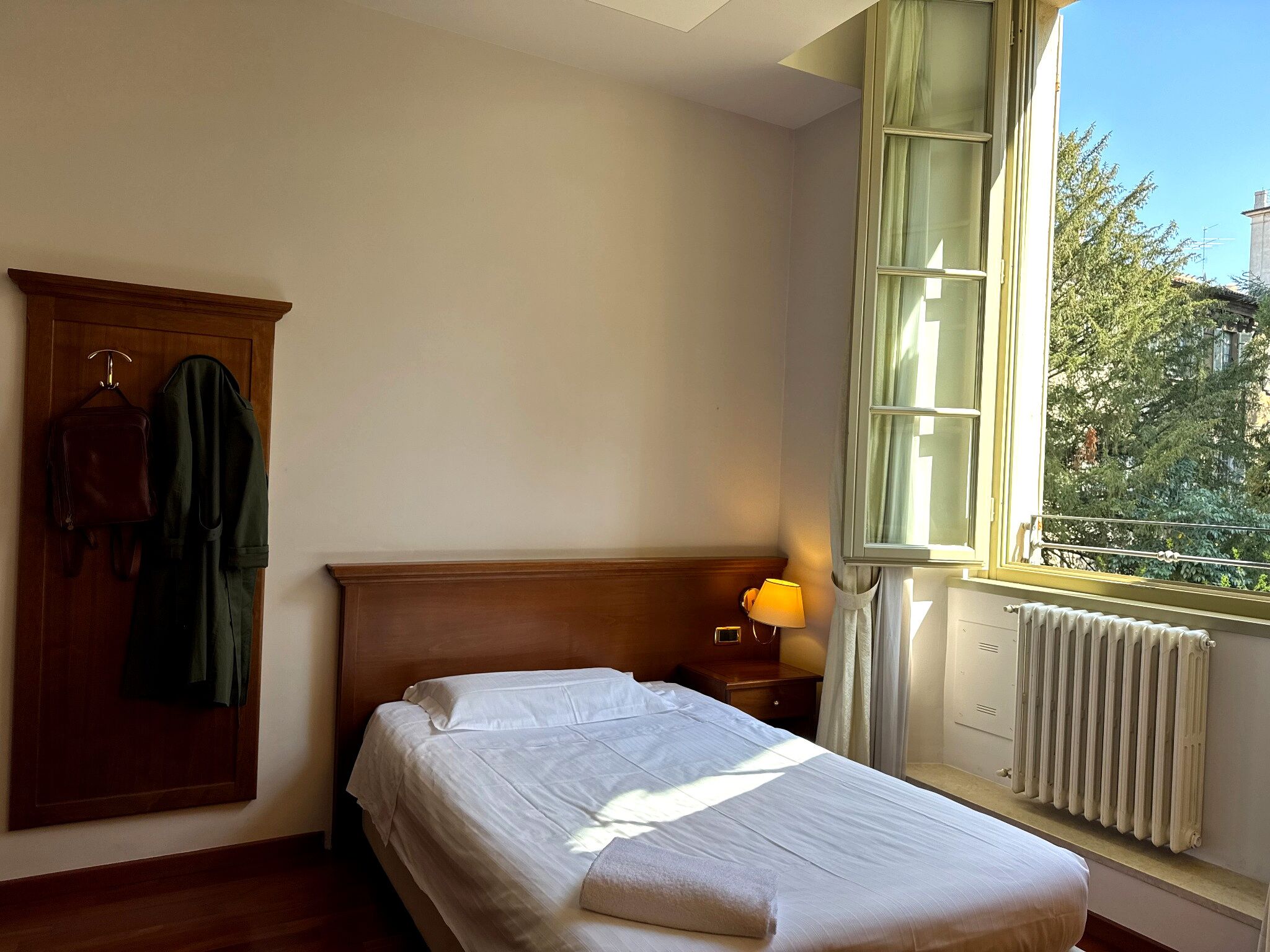 Un dormitorio con cama, armario de madera, ventana con vistas y radiador.