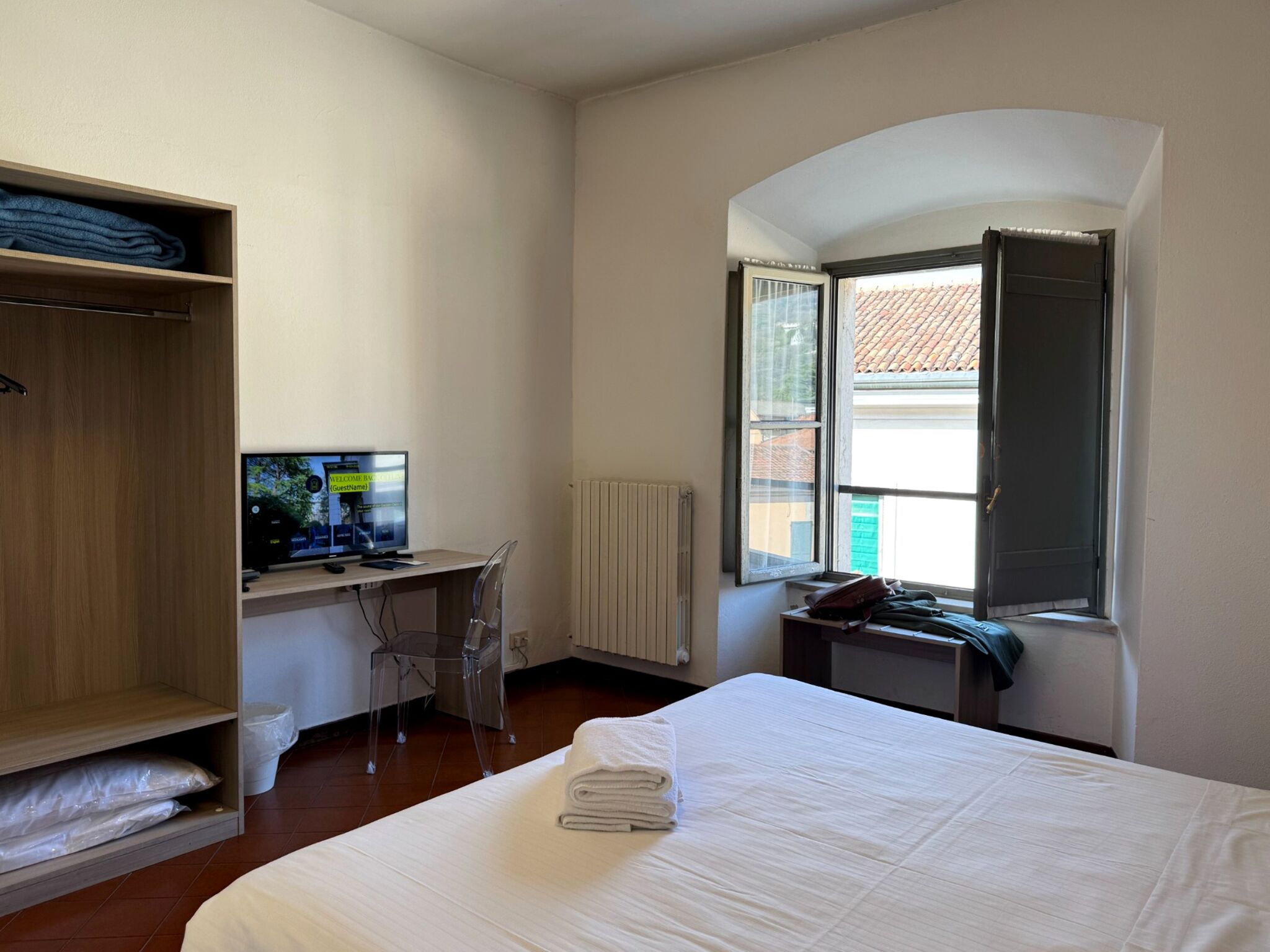 Ein Hotelzimmer mit Bett, Schreibtisch mit Computer, Kleiderschrank und Fenster mit geöffnetem Vorhang.