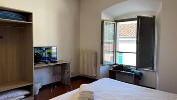 Ein Hotelzimmer mit Bett, Schreibtisch mit Computer, Kleiderschrank und Fenster mit geöffnetem Vorhang.