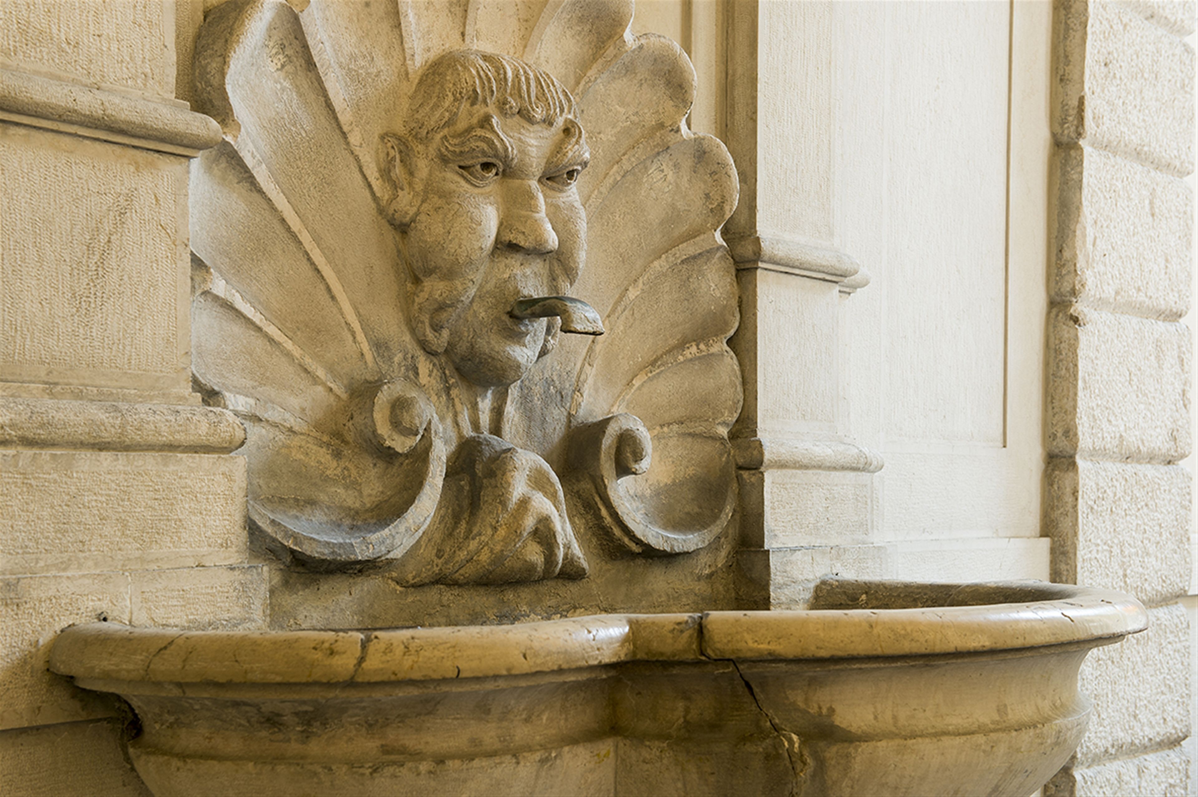 A stone architectural detail with a carved face and a decorative basin.