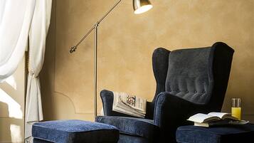 A room with a dark blue armchair, a matching ottoman, a floor lamp, and a small table with a book and a glass of juice.