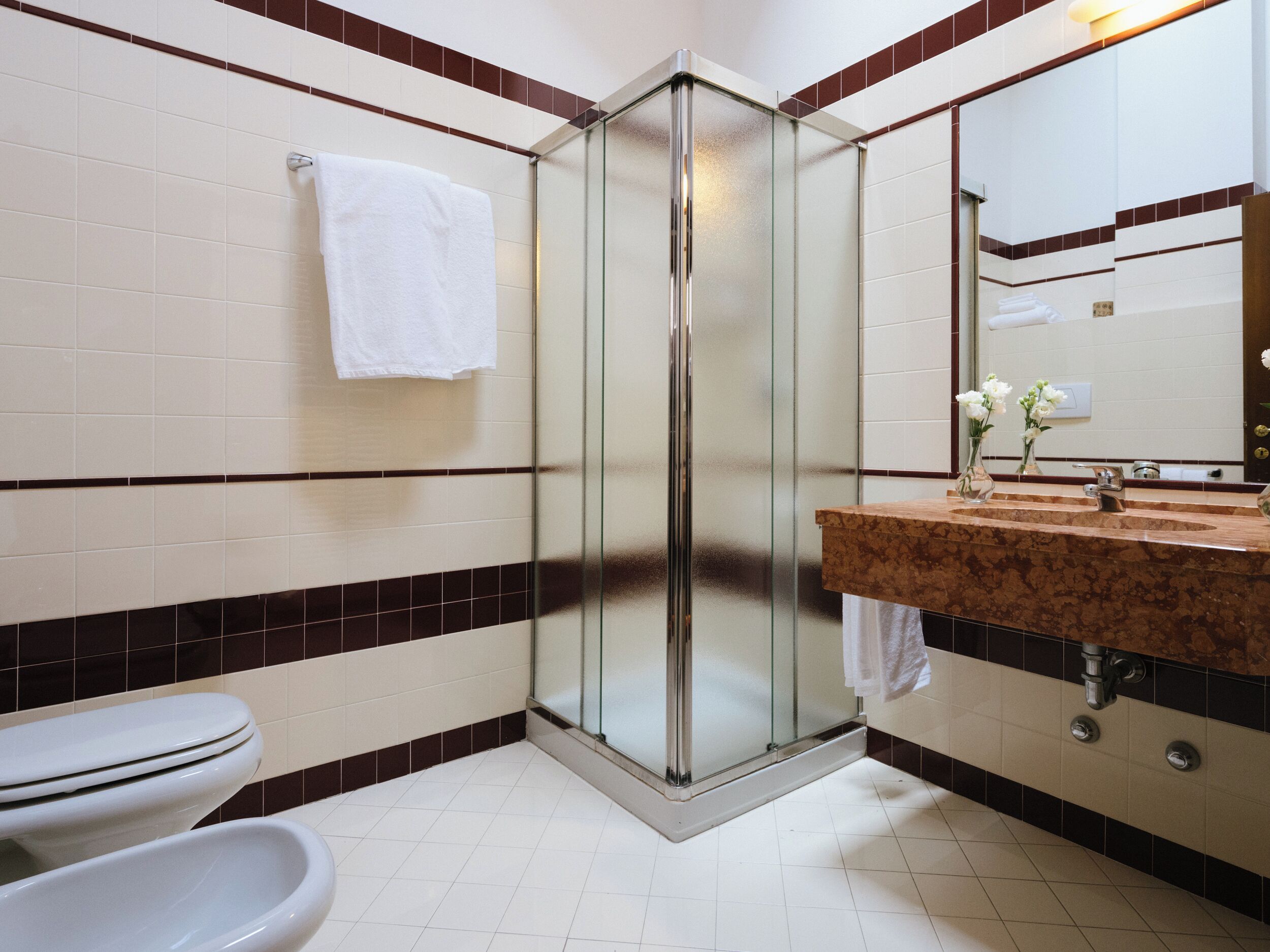 Un baño con cabina de ducha de vidrio, un lavamanos con encimera de mármol y un inodoro.