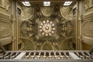 Un intérieur richement décoré, avec un lustre central, des sculptures complexes ornant les murs et une conception architecturale symétrique.