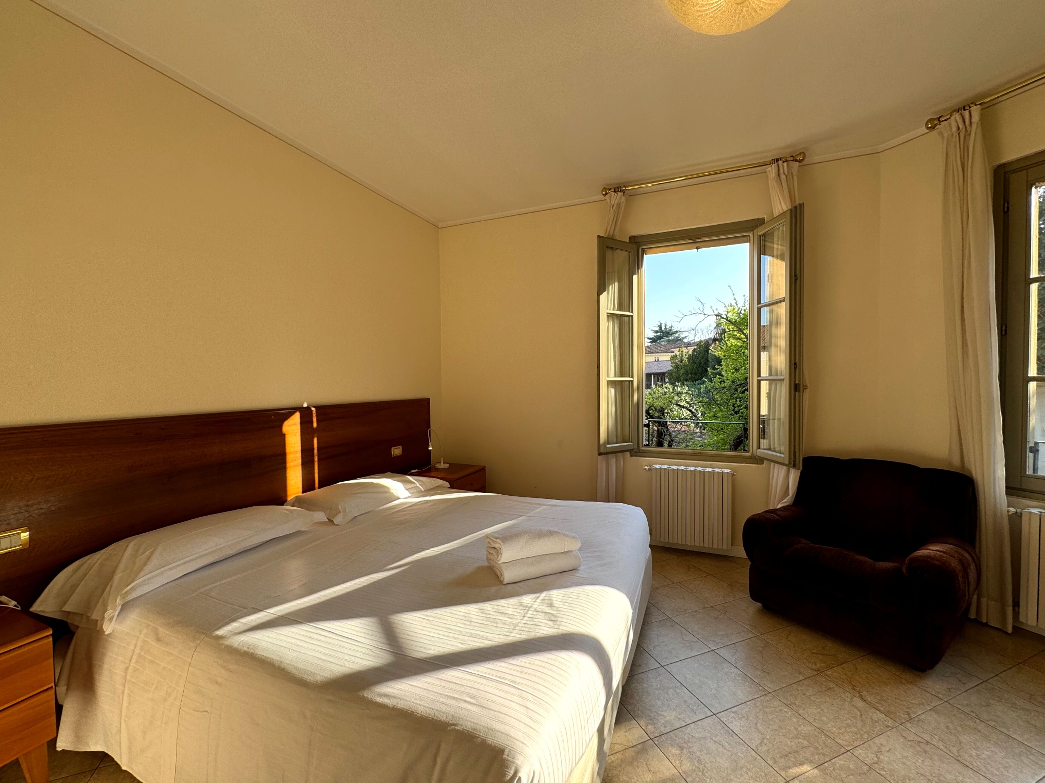 Habitación de hotel con una cama grande, una silla, una mesita de noche, una ventana con cortinas y un radiador.