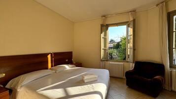 A hotel room with a large bed, a chair, a nightstand, a window with curtains, and a radiator.