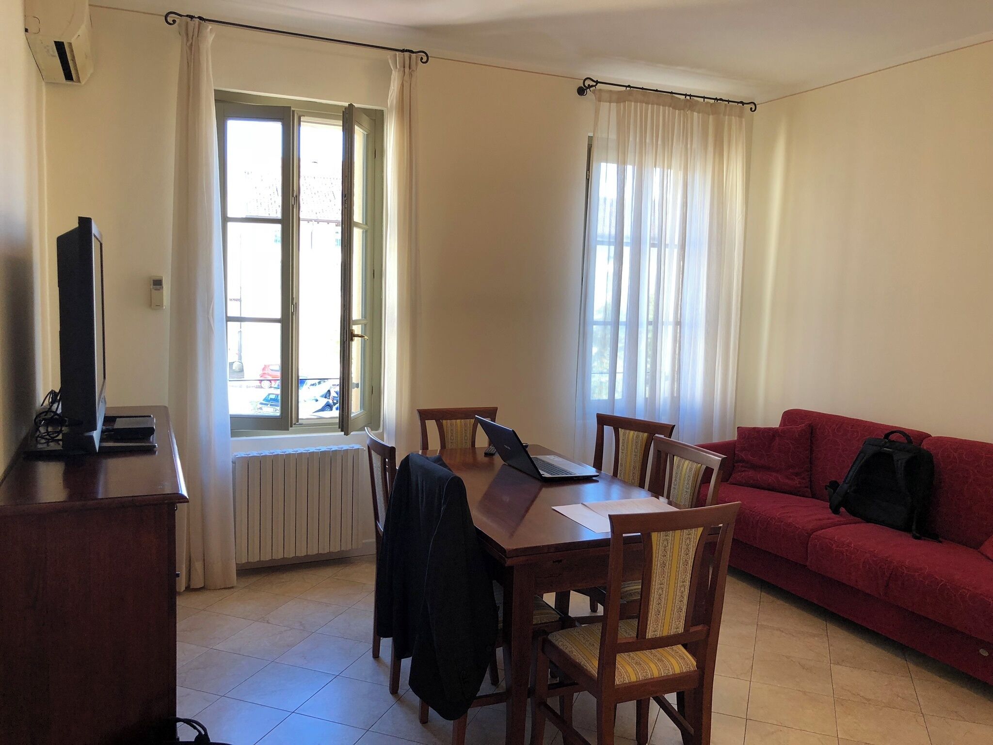 A room with a dining table, chairs, a red sofa, and a TV on a stand.