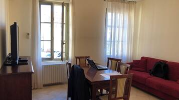 A room with a dining table, chairs, a red sofa, and a TV on a stand.