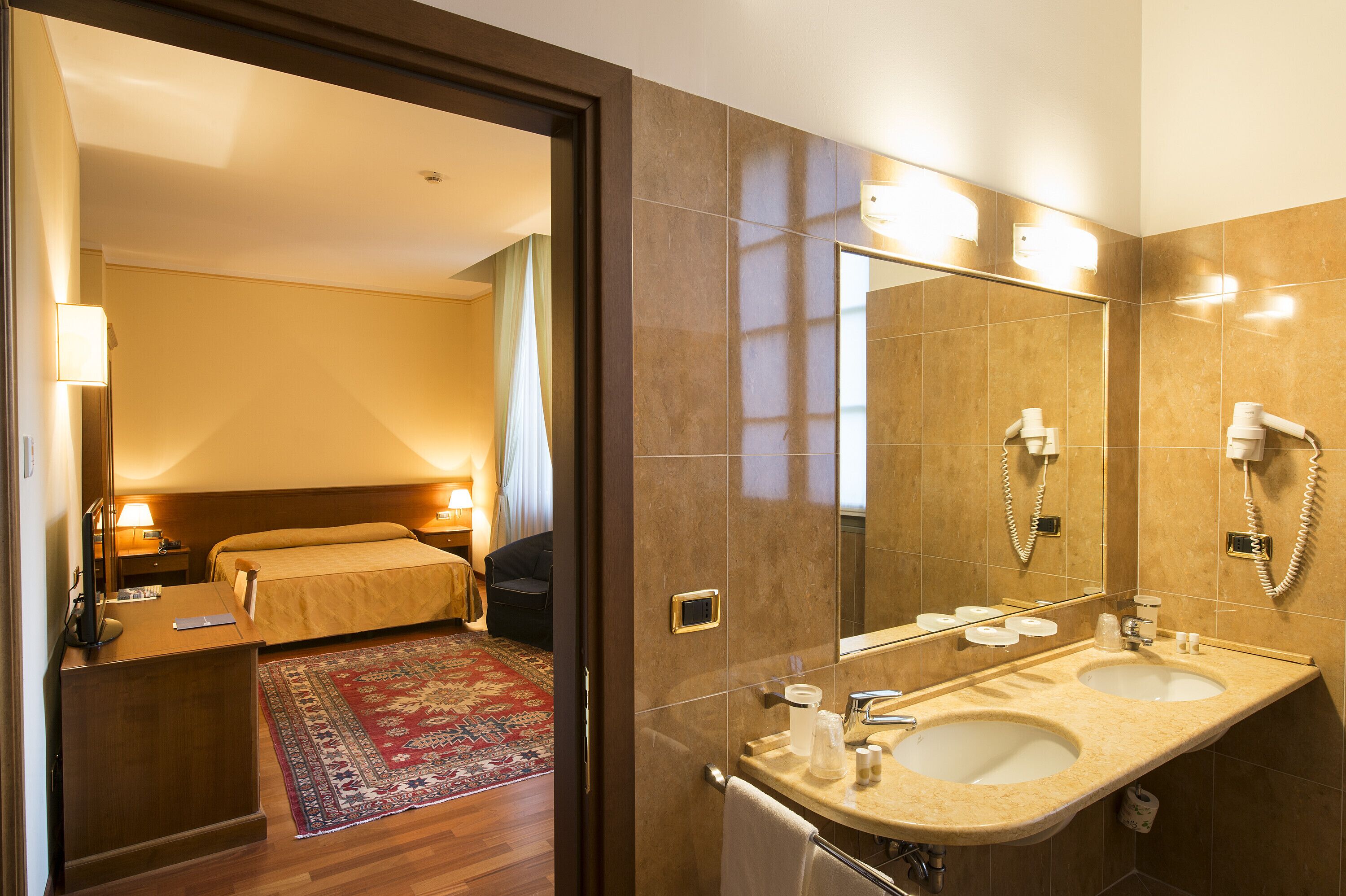 Un baño de hotel con un lavamanos doble, un espejo grande y una cama con alfombra roja.