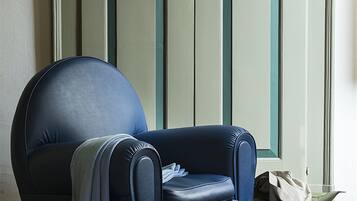 A room with a blue armchair, a stack of books, and a bag on the floor.