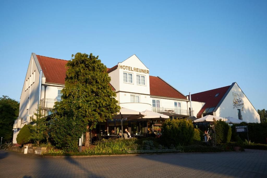 Et hotel med rødt tag, udendørs siddepladser og et skilt med teksten 'HOTELREUNER'.