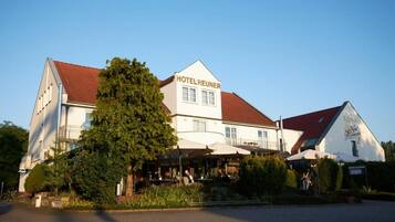 Et hotel med rødt tag, udendørs siddepladser og et skilt med teksten 'HOTELREUNER'.