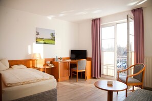 A hotel room with a bed, desk, chair, television, and a balcony with curtains. - Flair Hotel Reuner (Zossen)