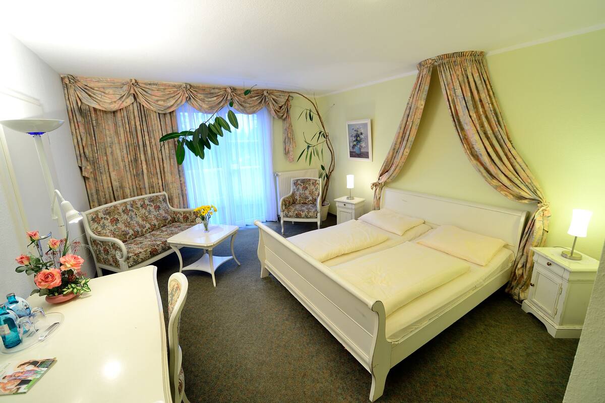 A hotel room with a bed, two chairs, a table, a lamp, and a plant.