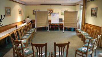 Un salón de conferencias con una larga mesa, filas de sillas y dos pantallas de proyección.